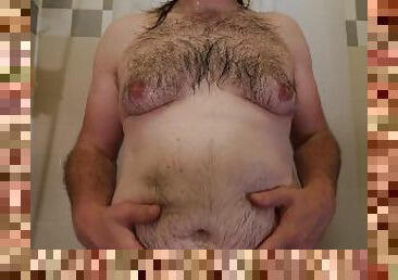 Close up of obese hairy man torso while standing naked in bathtub rubbing or massaging his belly